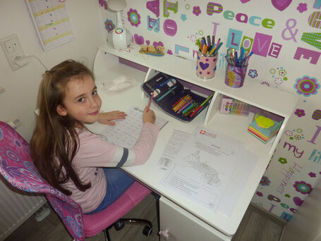 Das Foto (Nico Vogt) zeigt: Lara Vogt (Klasse 2) am Schreibtisch ihres Kinderzimmers beim Bearbeiten der Arbeitsblätter. Auf dem Tisch weitere Unterlagen aus dem Lernpaket.