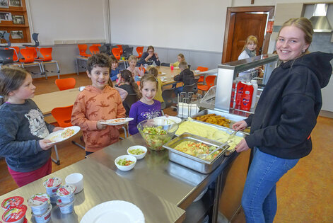 (Foto: Bulk) Die Mittagspause in der schuleigenen Mensa können die Kinder kaum erwarten. Sie freuen immer besonders, wenn Emma Rehrmann das leckere Essen auf die Teller füllt.  